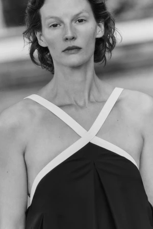 Close-up portrait of a female model wearing a black halter top with white criss-cross straps against an out-of-focus background.