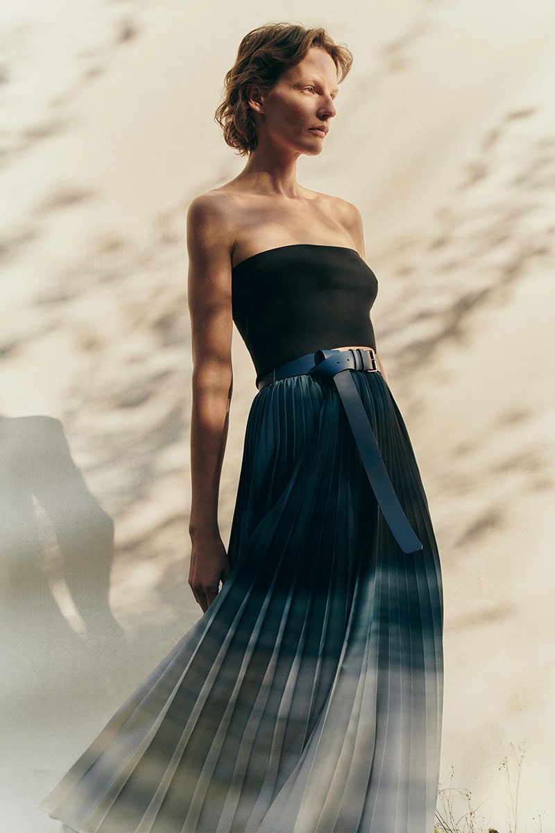 Model wearing a black bandeau top and pleated ombré skirt with a wide belt against a light textured background.