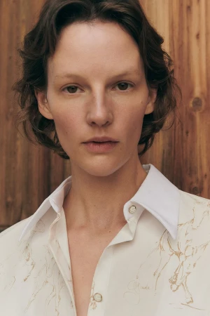 Close-up portrait of model Sara Blomqvist wearing a printed shirt against a wooden plank wall for Giada Leisure campaign