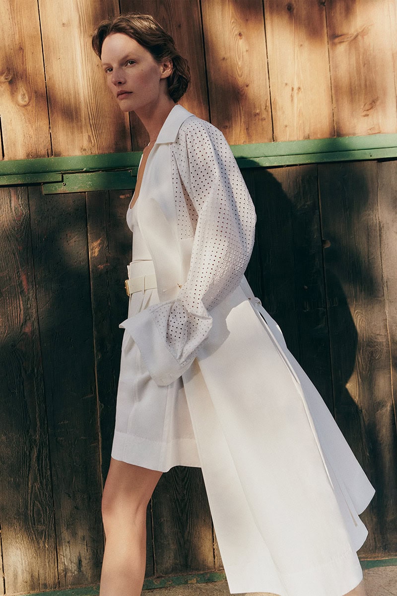 Model Sara Blomqvist in a white belted coat against a dark wood wall for Giada Leisure campaign