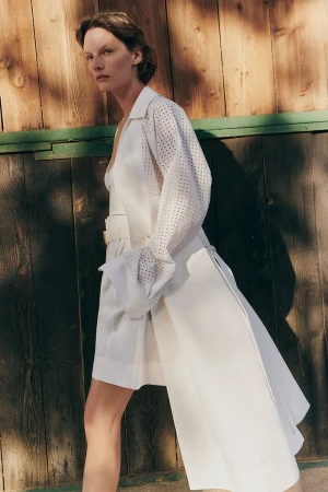 Model Sara Blomqvist in a white belted coat against a dark wood wall for Giada Leisure campaign