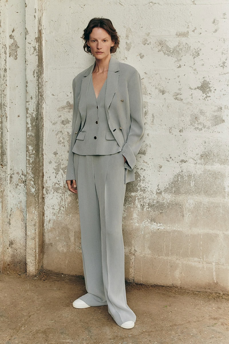 Model Sara Blomqvist in a grey trouser suit and vest standing against a textured concrete wall for Giada Leisure campaign
