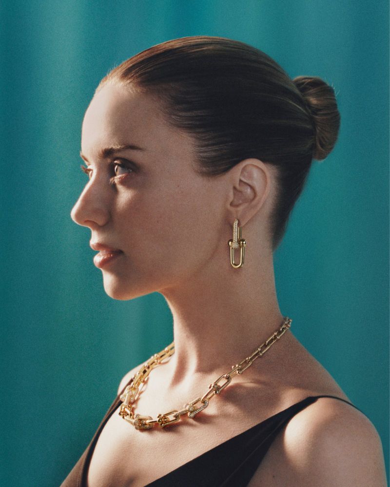 Profile portrait of a woman wearing gold chain jewelry against a textured turquoise background for Tiffany and Co.