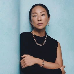 Portrait of a woman wearing gold chain jewelry and a black top against a textured blue background