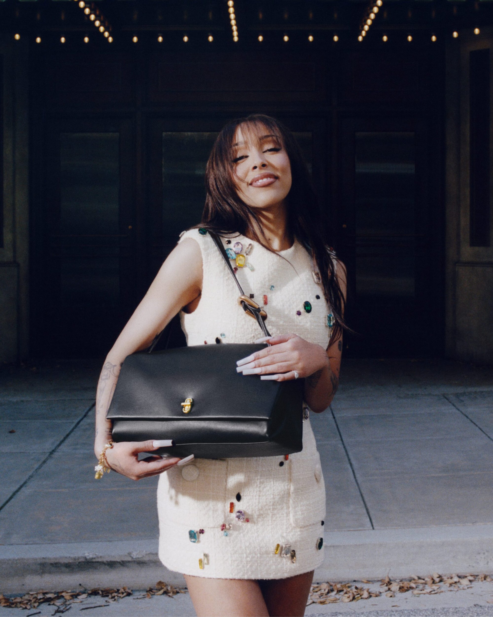 Doja Cat wearing an embellished white dress holding a black leather handbag outdoors for Marc Jacobs