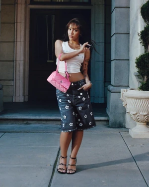 Doja Cat wearing a white tank top and floral denim shorts holding a pink handbag outside a building for Marc Jacobs