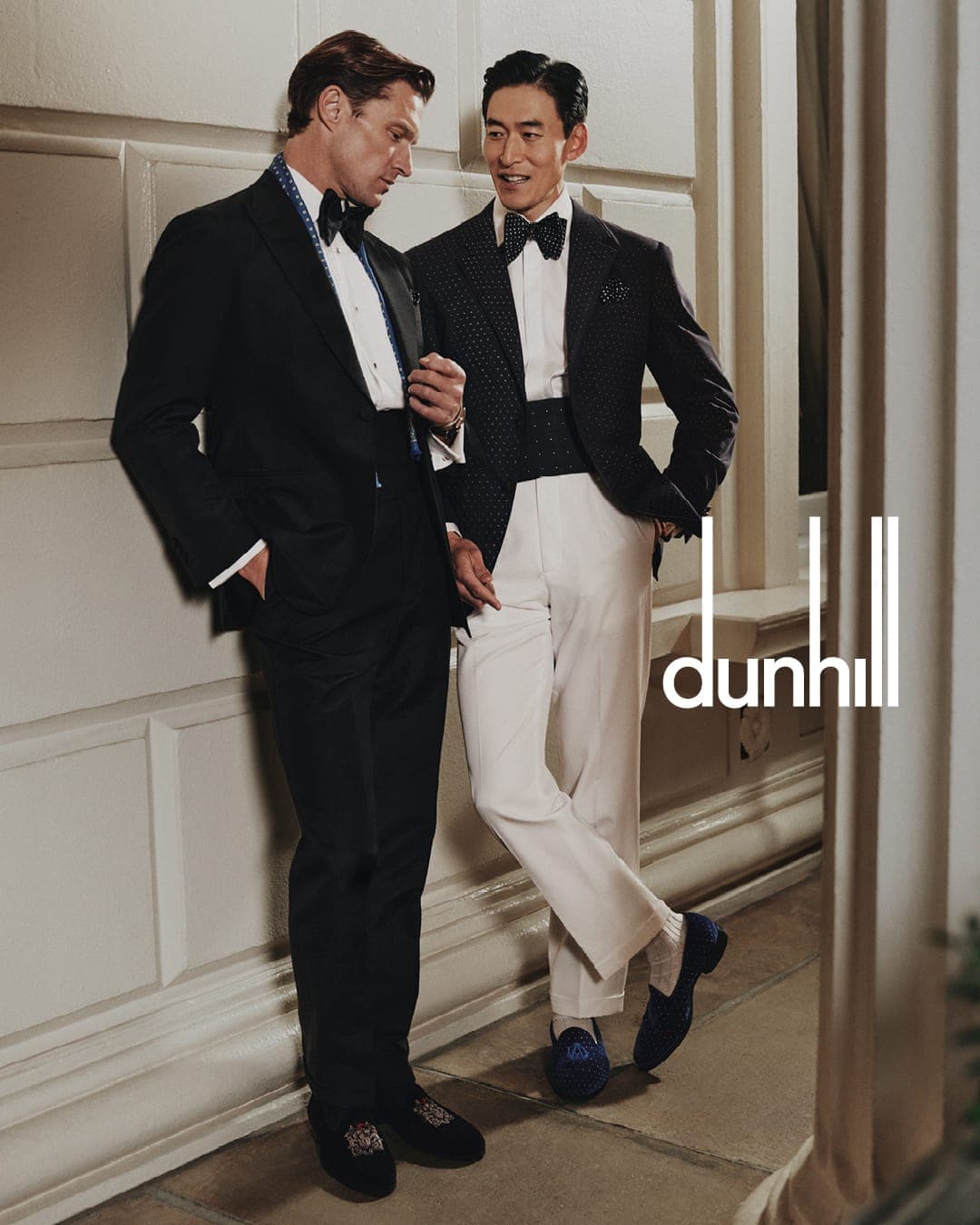 Two men in formal black tie attire posing against a classic architectural wall for a Dunhill campaign.