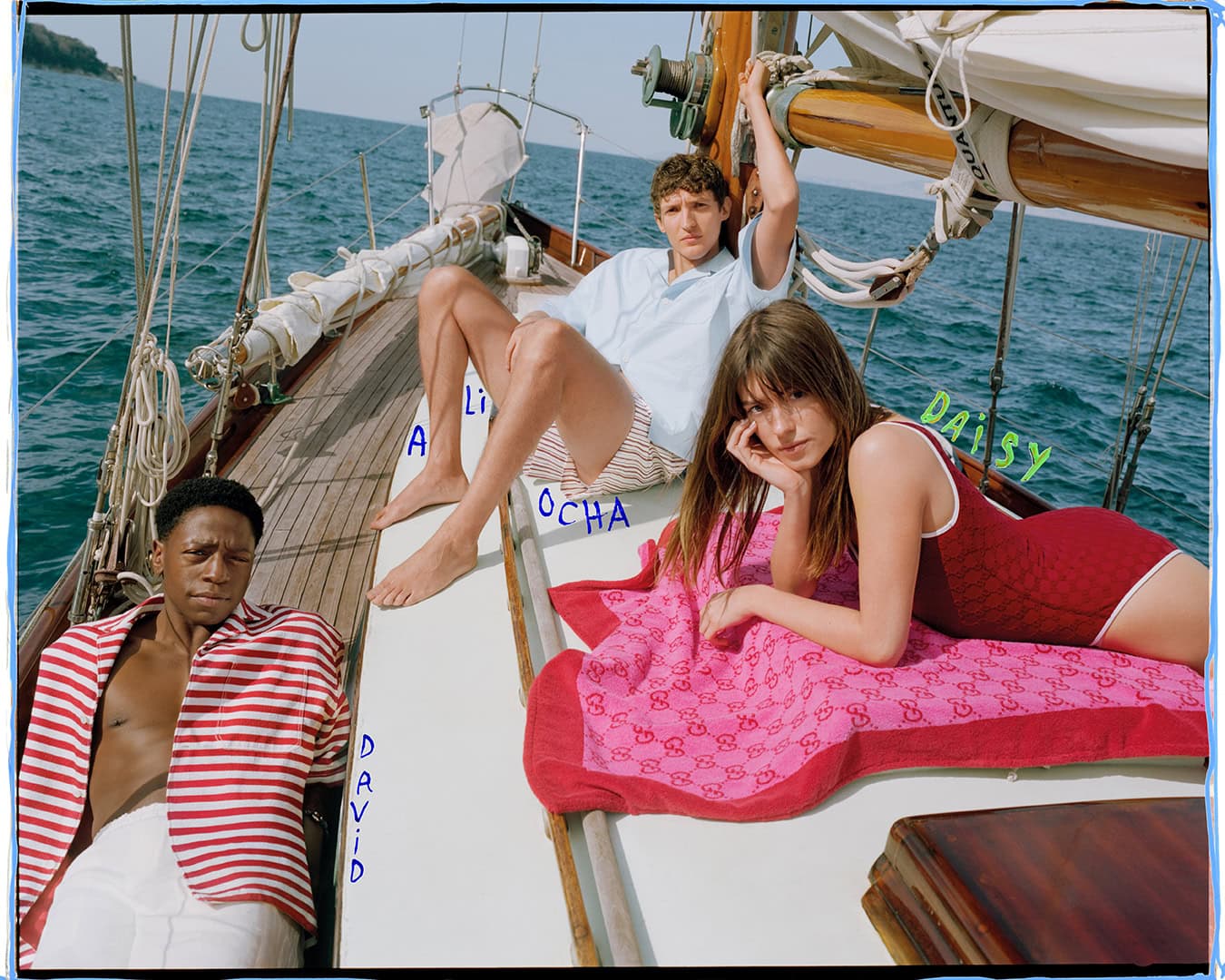 Three models lounging on the deck of a sailboat in the ocean for the Gucci Lido Spring 2025 campaign.