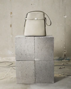Beige leather bucket bag resting on a square concrete block against a weathered wall background