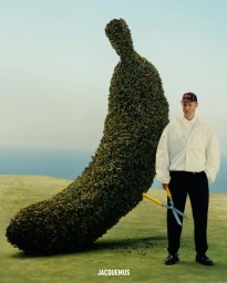 Man holding garden shears standing beside a giant banana-shaped topiary hedge on a green lawn