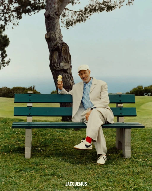 Jon Gries seated on a green park bench holding an ice cream cone for Jacquemus
