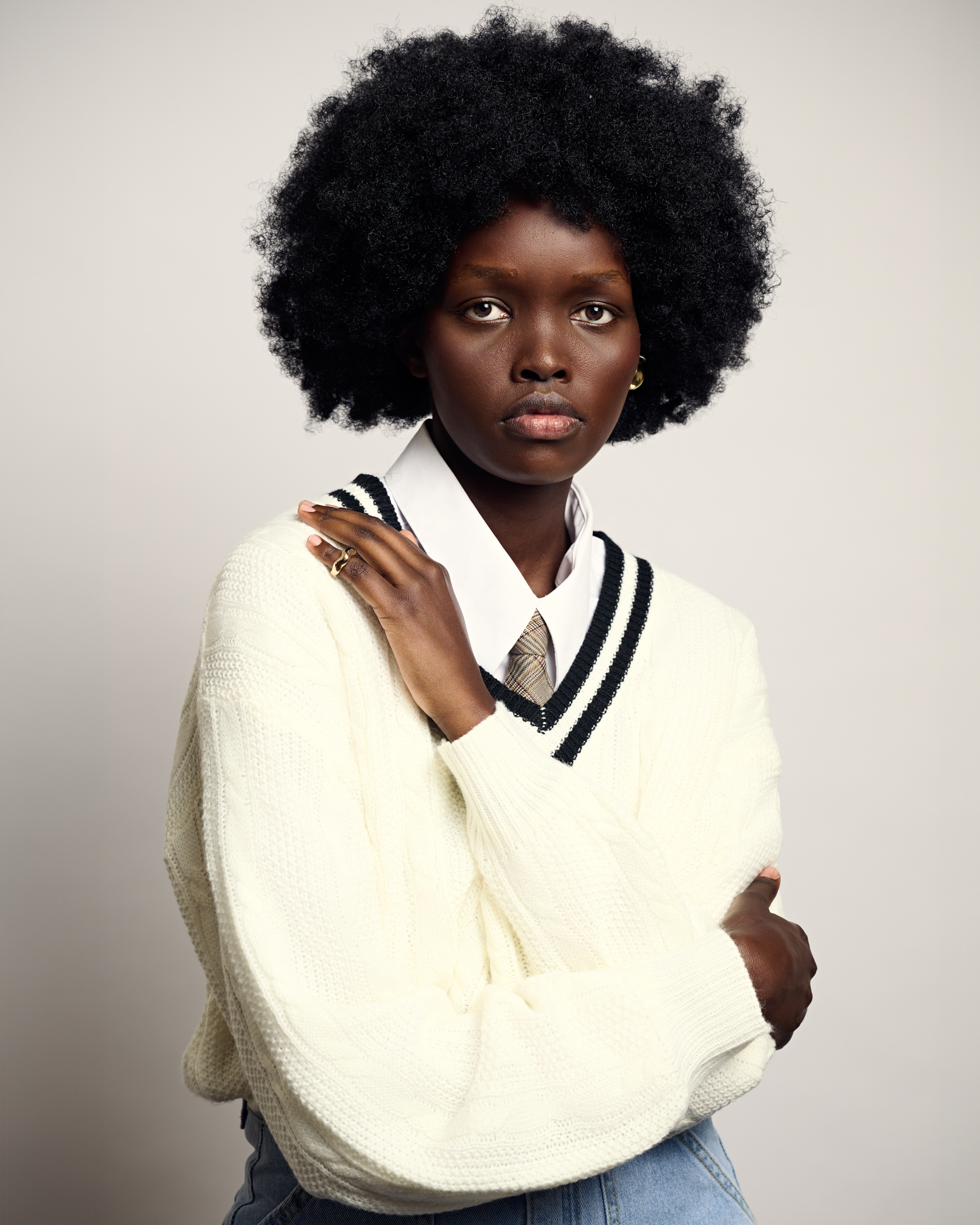 Portrait of a Black woman with an afro wearing a cream V-neck sweater and white collared shirt against a plain light background
