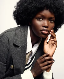 Close-up portrait of Goldah Tekeiwa in a grey wool coat, white collared shirt, and tie against a white seamless background