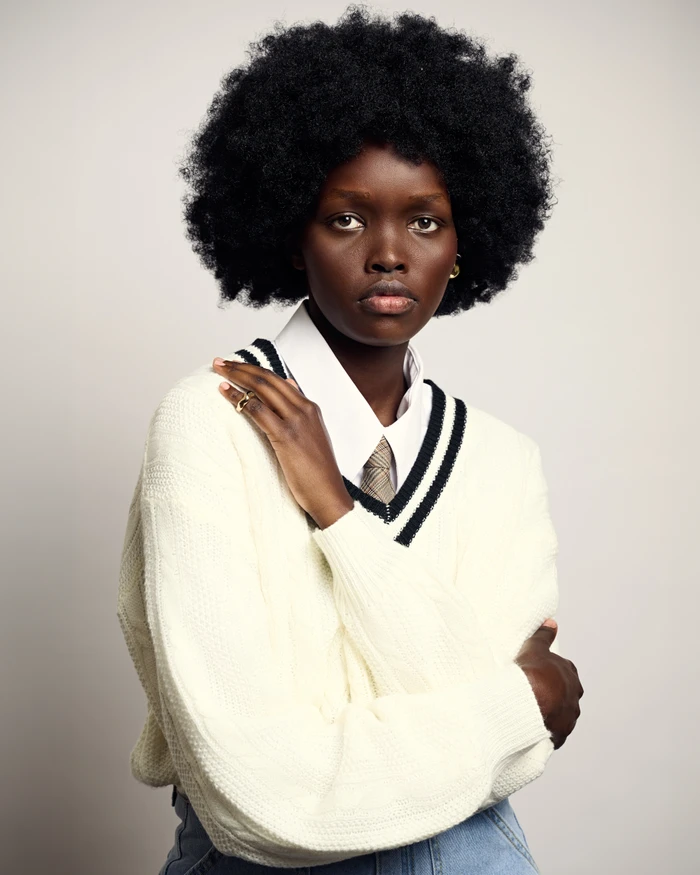 Portrait of a Black woman with an afro wearing a cream V-neck sweater and white collared shirt against a plain light background
