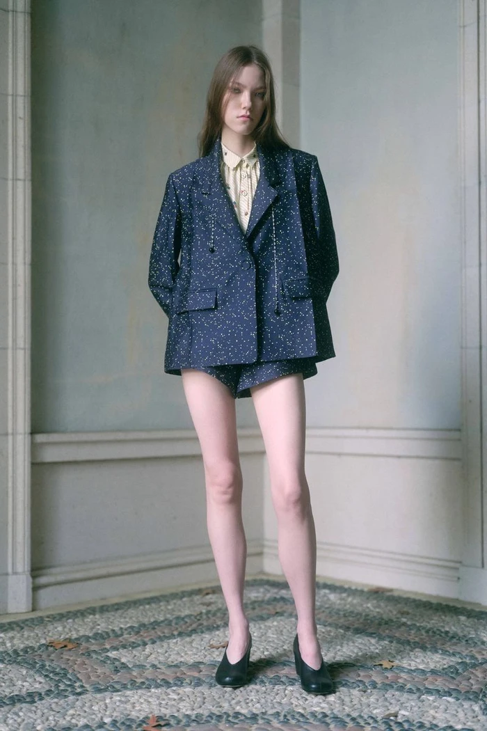 Model wearing a printed navy blazer and shorts against an interior architectural background