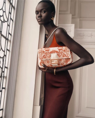 Model Achol Kuir holding a beaded Fendi handbag while posing near an arched window indoors