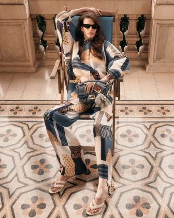 Model Achol Kuir seated in a lounge chair wearing patterned loungewear and holding a handbag for Fendi Summer 2025 ad campaign.