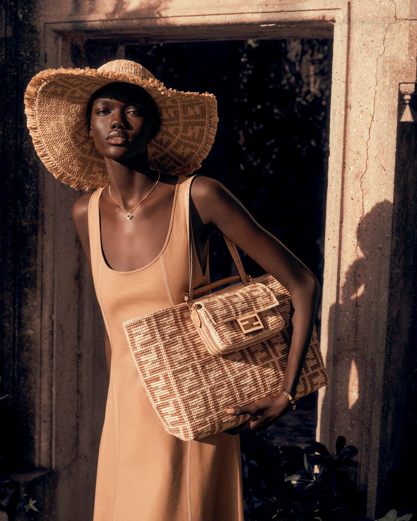 Model Achol Kuir wearing a straw sun hat and holding a woven Fendi tote bag for the Summer 2025 ad campaign.