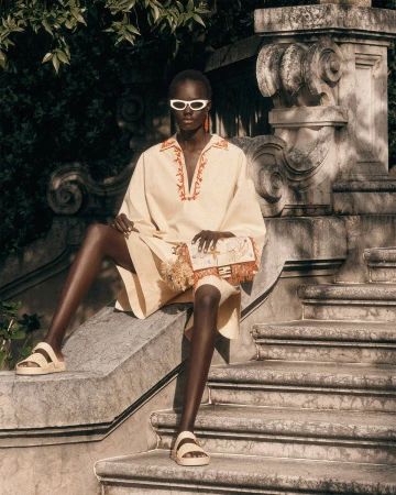 Model Achol Kuir in white sunglasses and cream tunic sitting on ornate stone steps for Fendi