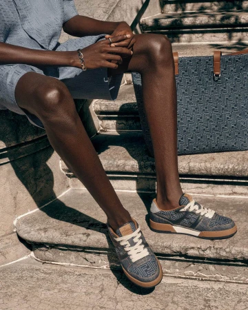 Model Achol Kuir wearing printed sneakers and seated on stone steps for the Fendi Summer 2025 Ad Campaign.