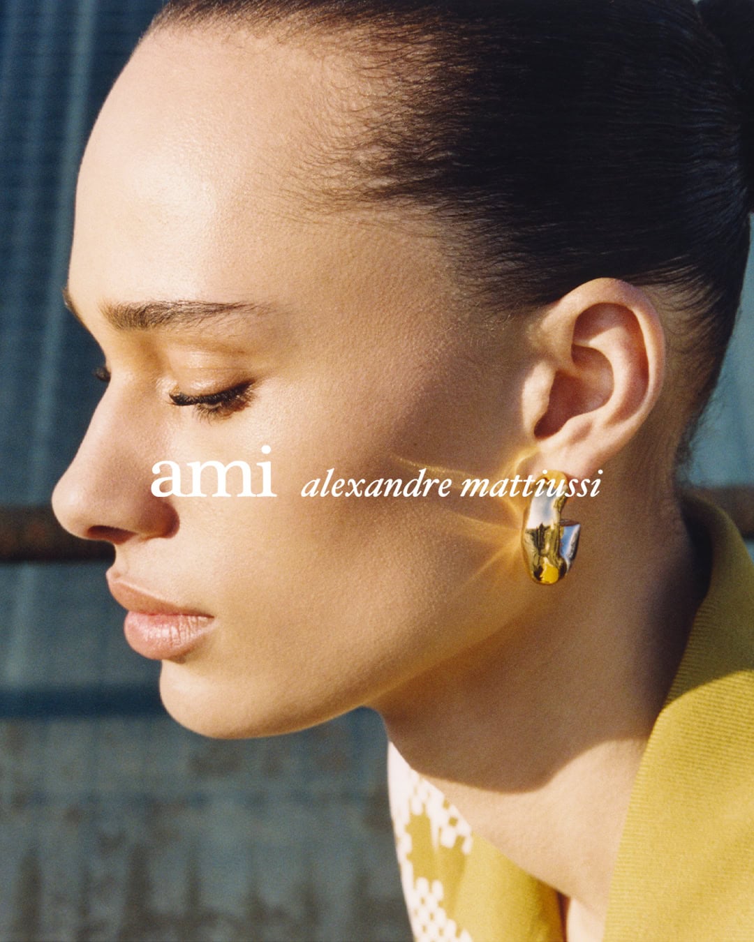 Close-up profile portrait of a model wearing a gold hoop earring and yellow top for the Ami Spring 2025 ad campaign.