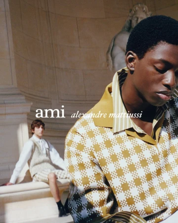 Black man in patterned shirt in the foreground with another man seated in the background against classical stone architecture