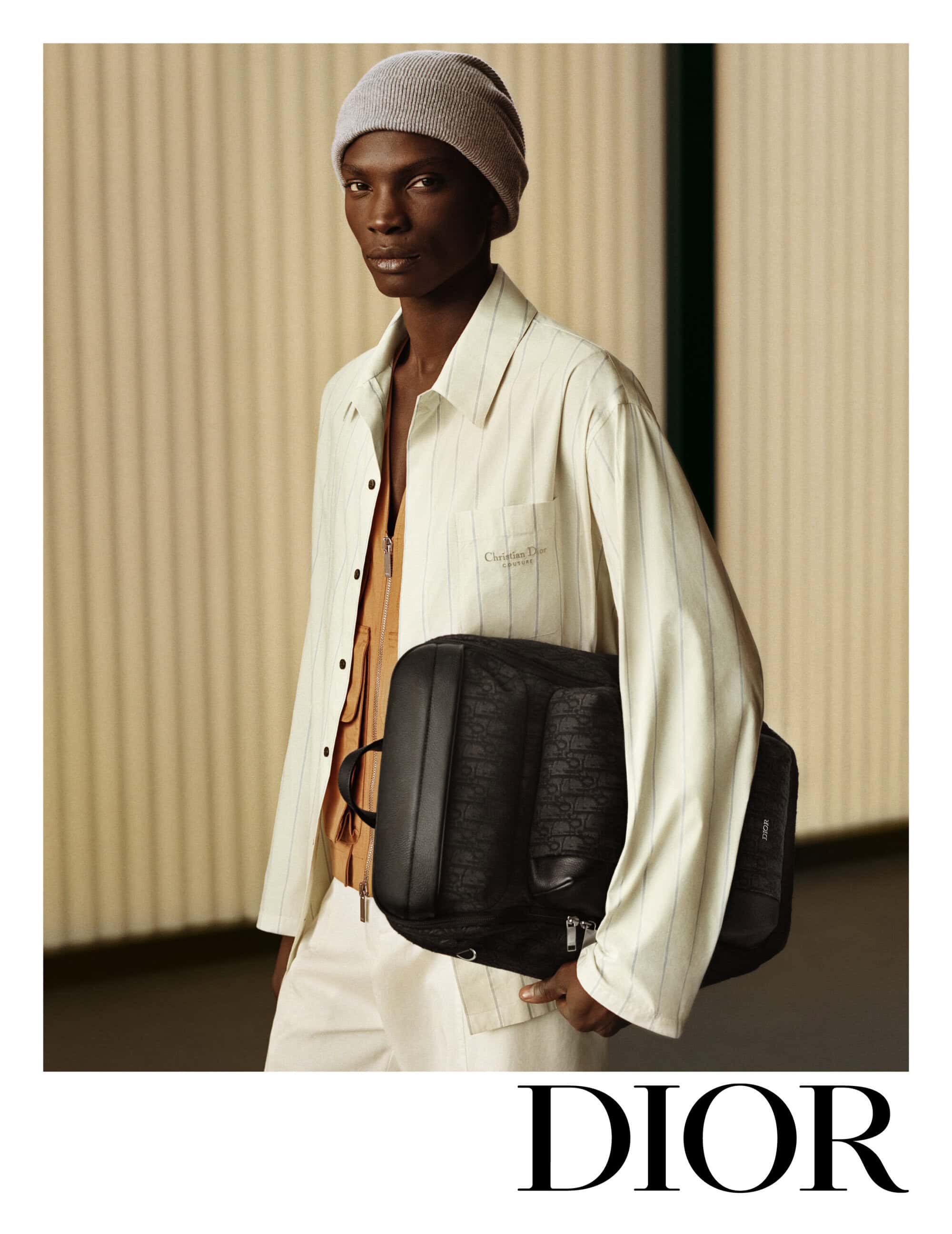 Model wearing white striped shirt and beanie holding black backpack for Dior campaign