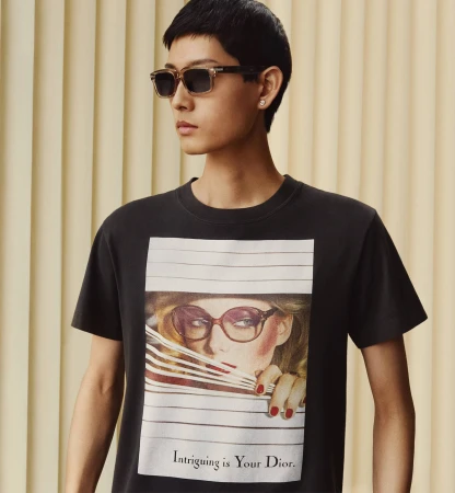 Model wearing dark sunglasses and graphic t-shirt standing against a vertical paneled background