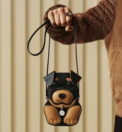 Close-up of a person holding a novelty dog-shaped leather crossbody bag against a vertical slatted background.