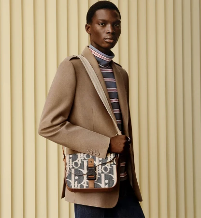 Black man wearing a camel blazer and monogram messenger bag against fluted wall