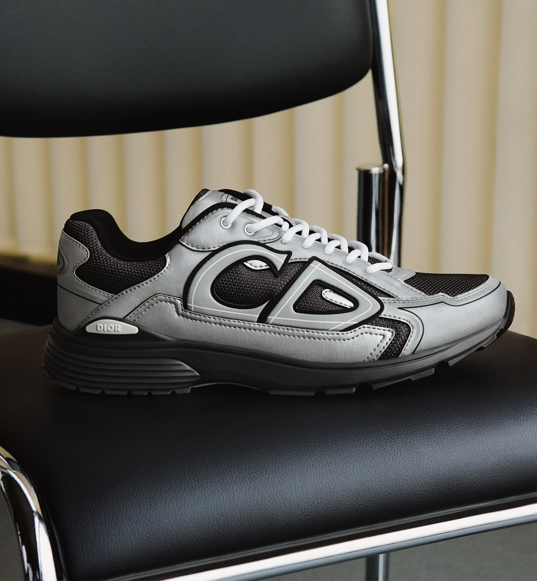 Silver and black designer sneaker resting on a black leather chair with chrome legs.