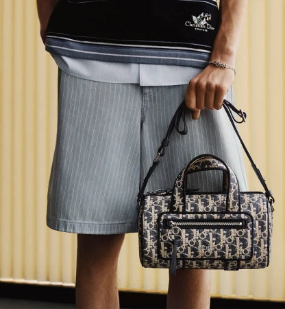 Model holding a monogram patterned handbag wearing pinstripe shorts and striped knit top for Dior Fall 2025 campaign.