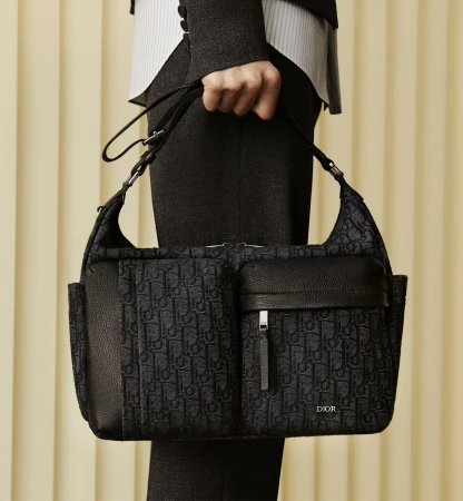 Close-up of a person holding a dark patterned shoulder bag with front pockets against vertical ribbed panels