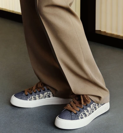 Close-up of designer sneakers with monogram pattern and thick brown laces worn with tailored trousers