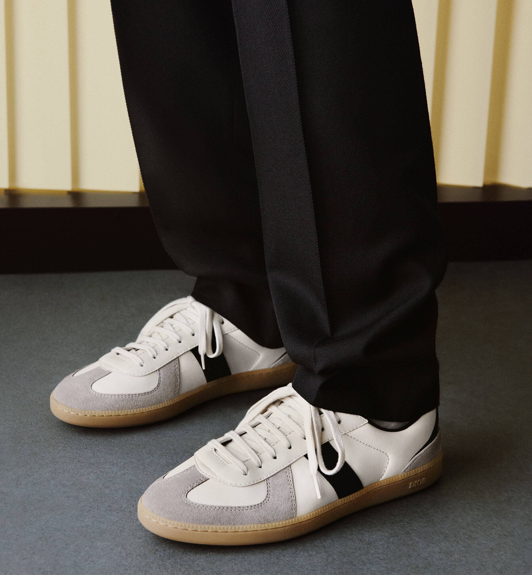 Close-up shot of white and grey sneakers with dark trousers for the Dior Men Fall 2025 campaign.