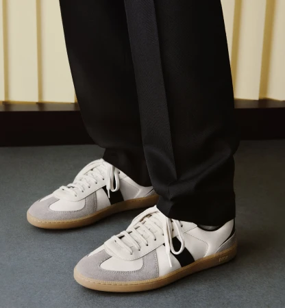 Close-up shot of white and grey sneakers with dark trousers for the Dior Men Fall 2025 campaign.