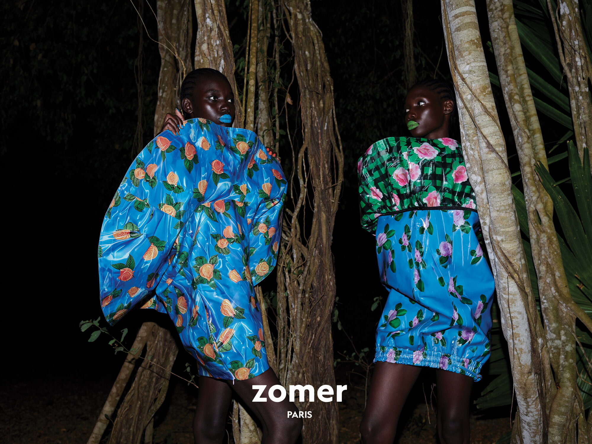 Two black female models in sculptural floral dresses posing among dark forest trees at night for Zomer campaign