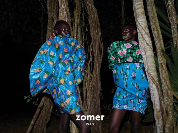Two black female models in sculptural floral dresses posing among dark forest trees at night for Zomer campaign