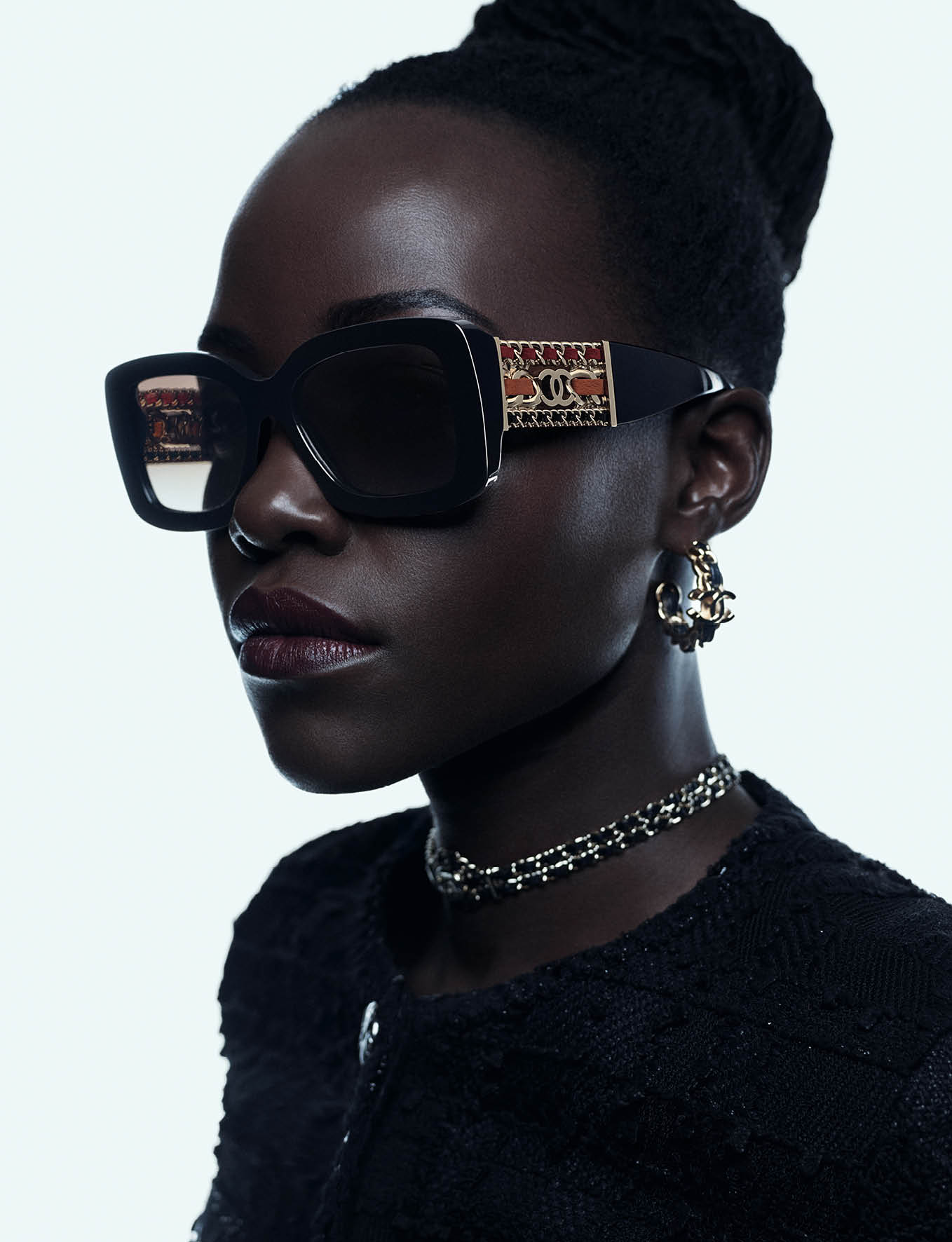 Close-up portrait of Lupita Nyong'o wearing black sunglasses and a black textured top against a bright white background.