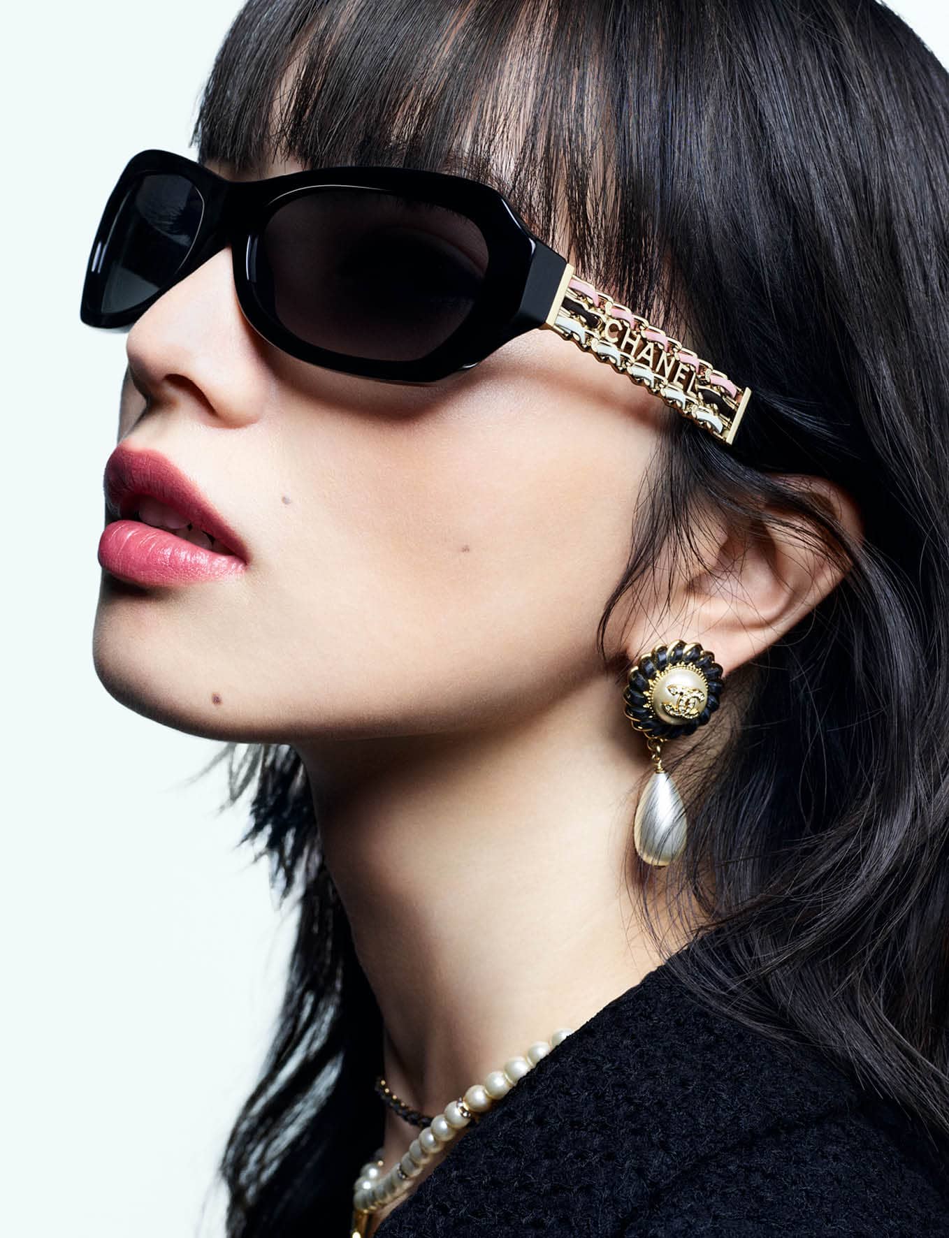Close-up portrait of model Nana Komatsu wearing black sunglasses and pearl earrings against a white background