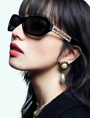 Close-up portrait of model Nana Komatsu wearing black sunglasses and pearl earrings against a white background