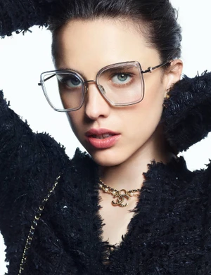 Model wearing clear frame glasses and a black tweed jacket against a white background for Chanel Eyewear Spring 2025 campaign.