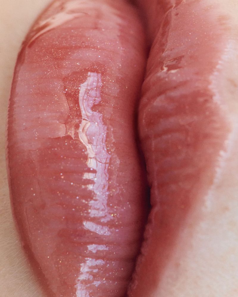 Close-up shot of a person's glossy, pink lips, highlighting the texture and subtle details of the lip's surface, with a blurred background.