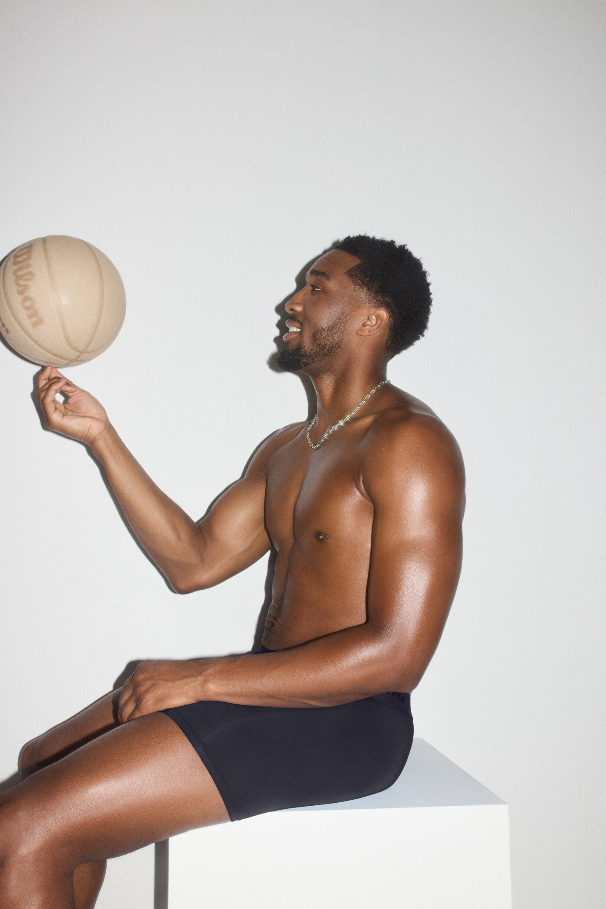Model Donovan Mitchell spinning a basketball on his finger against a seamless white studio background for SKIMS.
