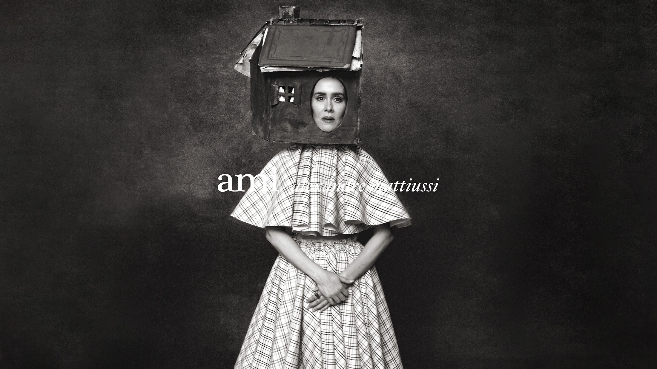 Model Sarah Paulson wearing a miniature house structure on her head and a plaid cape outfit for Ami.