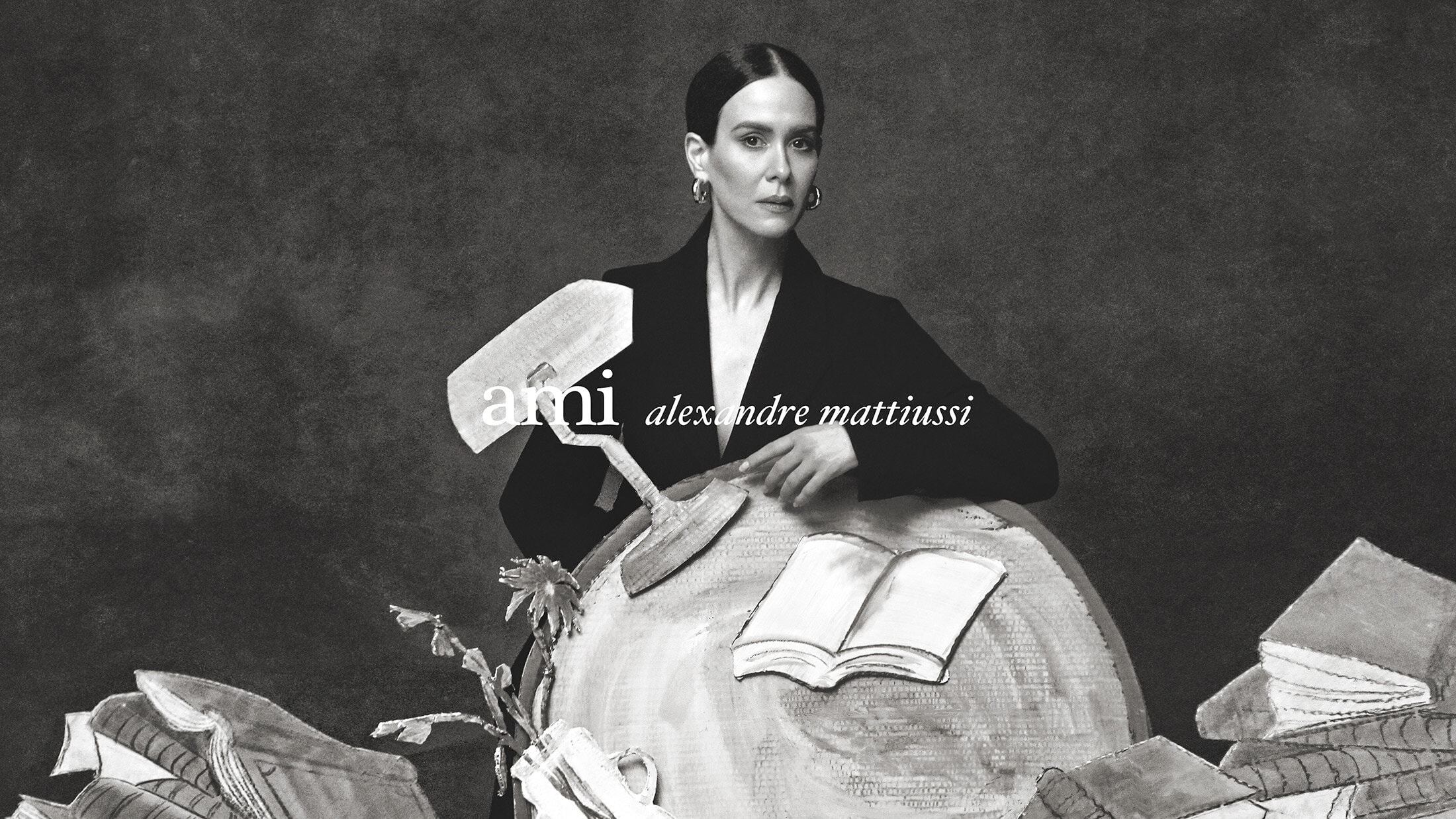 Model Sarah Paulson wearing a black blazer behind illustrative set props for Ami Spring 2025 campaign