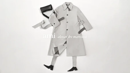 Flat lay composition of an Ami trench coat, black handbag, and boots against a plain white background