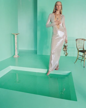 Model Abby Champion wearing a long sparkly sequin gown standing on a mint green studio floor next to a sunken pool.