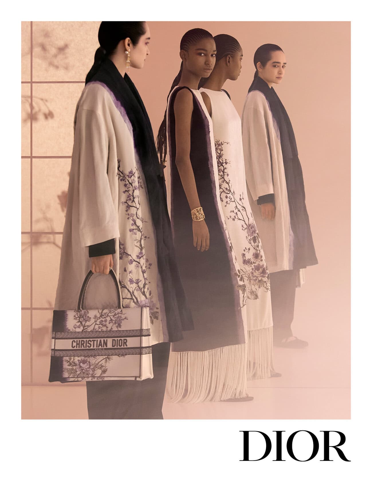 Four models in embroidered coats and dresses posing against a warm peach backdrop with floral shadow patterns, holding a Dior tote bag.