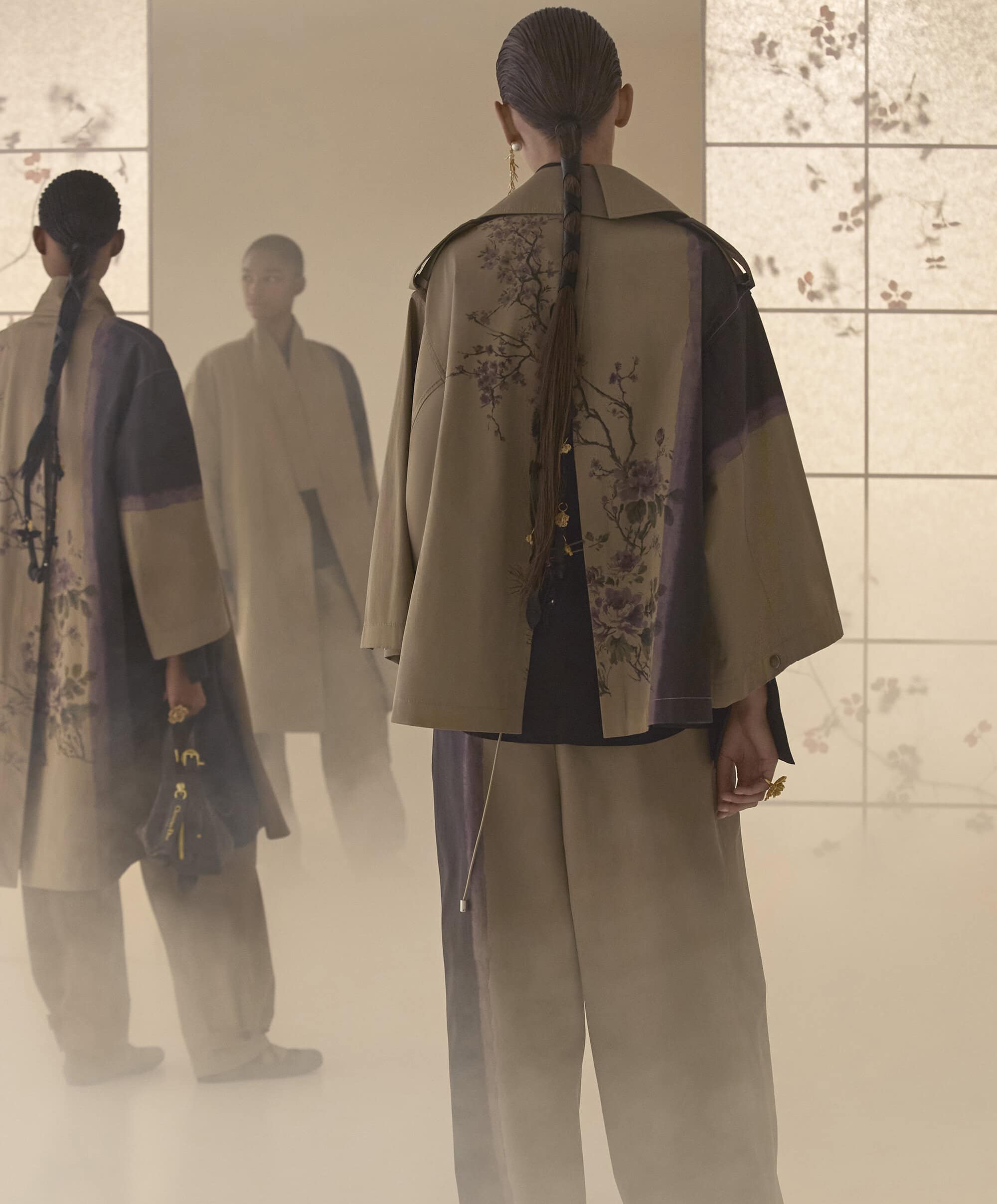 Model seen from behind wearing an embroidered floral jacket and trousers with hair styled in a long braided ponytail.